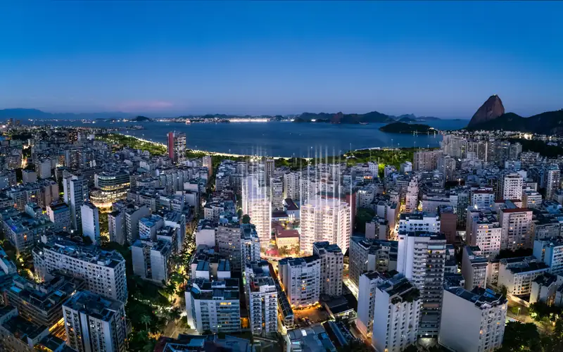 Vista aérea panorâmica do bairro do Flamengo, destacando o Aterro, a Marina da Glória e o Pão de Açúcar ao fundo durante o entardecer.